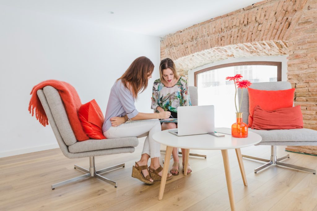 Two women sitting on a couch, focused on a laptop, engaged in conversation and sharing ideas