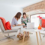 Two women sitting on a couch, focused on a laptop, engaged in conversation and sharing ideas